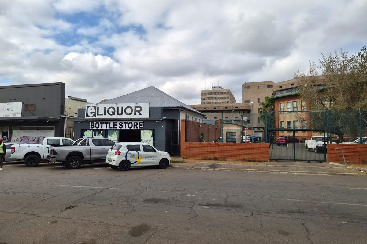 Street-level view of a retail liquor store property featuring a metal roof, brick boundary wall, and gated access to the rear parking area.