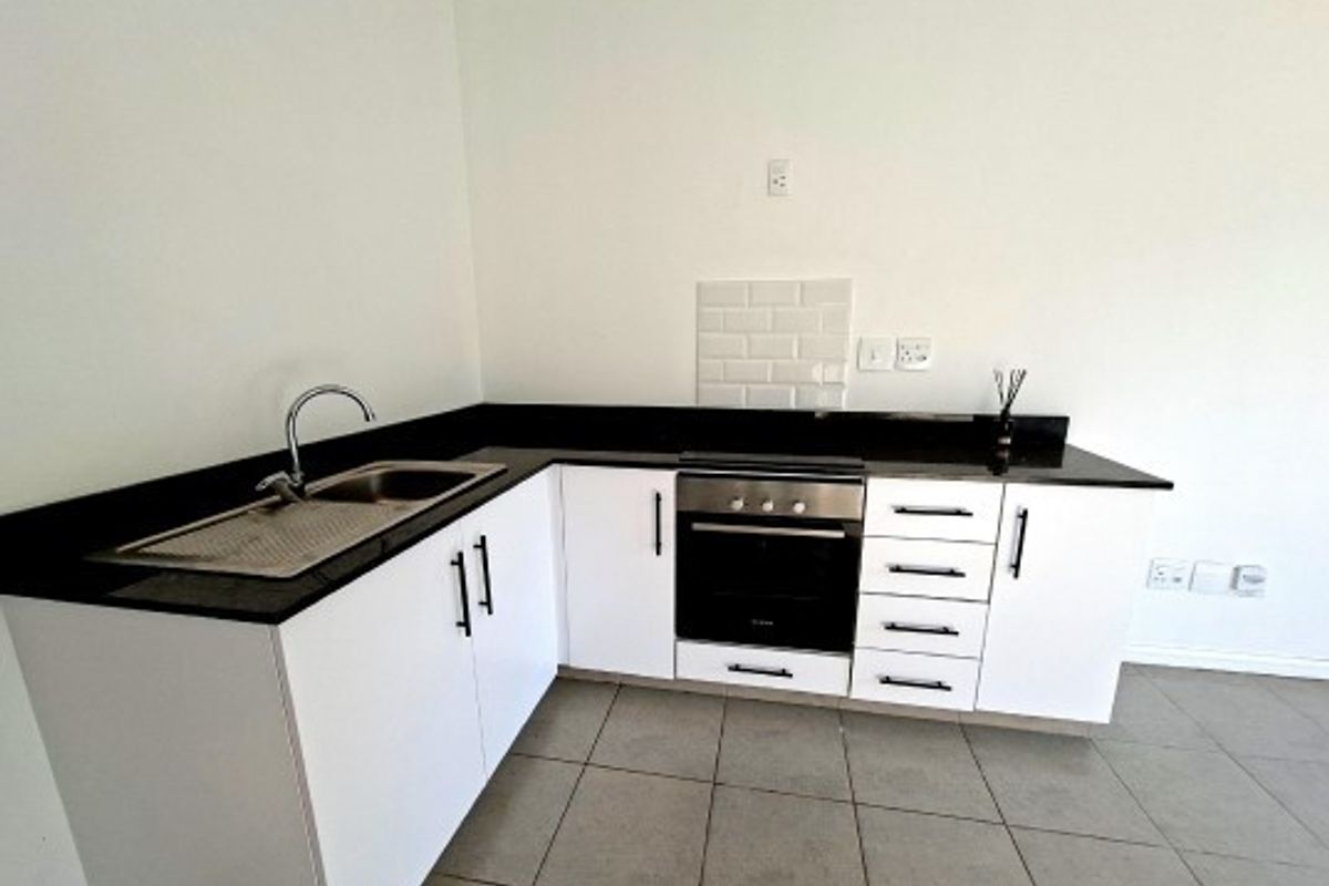A clean, modern kitchen featuring white cabinetry, dark countertops, a built-in oven, and a subway tile splashback with neutral tiled flooring.
