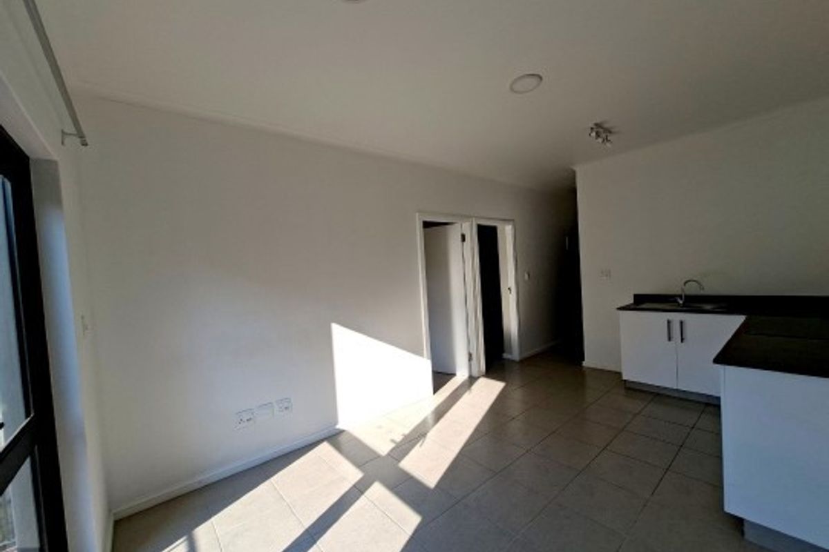 An open-plan living and kitchen area featuring tiled flooring, recessed lighting, and modern built-in kitchen cabinetry with a sink.