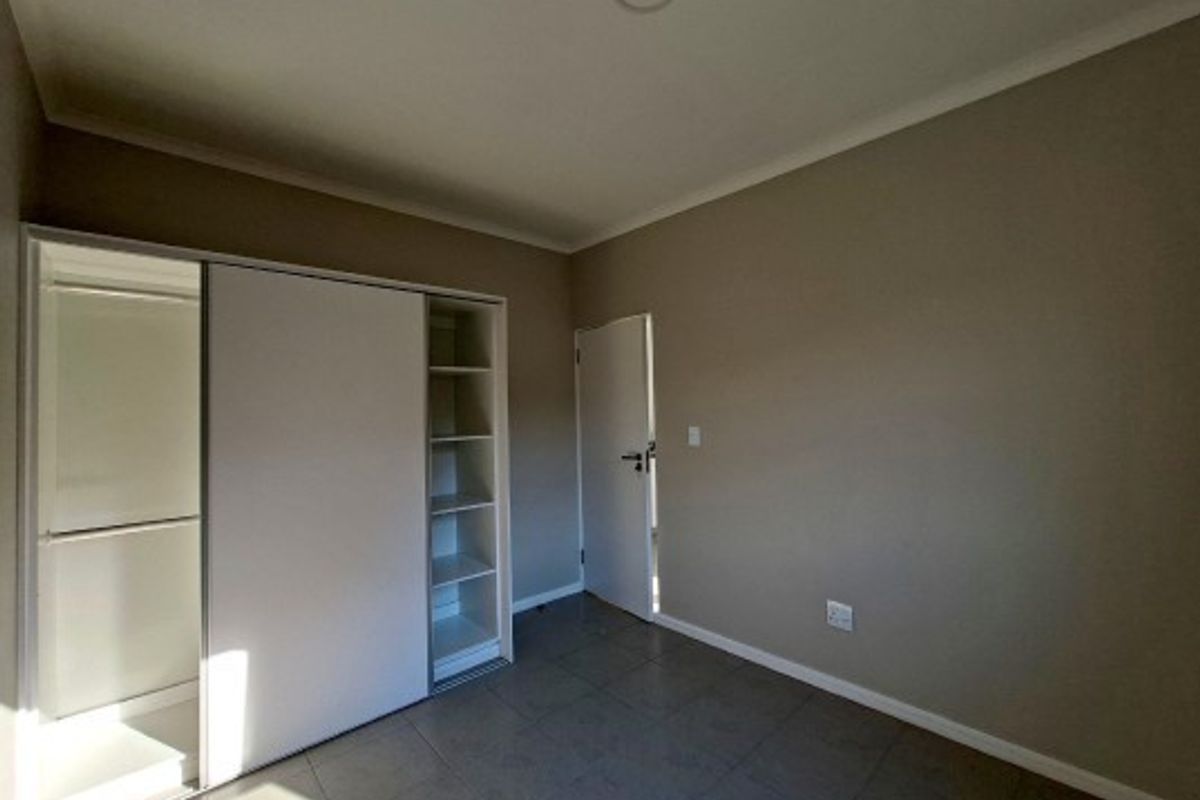A clean, empty bedroom featuring neutral wall tones, tiled flooring, and a functional built-in sliding door wardrobe with integrated shelving.