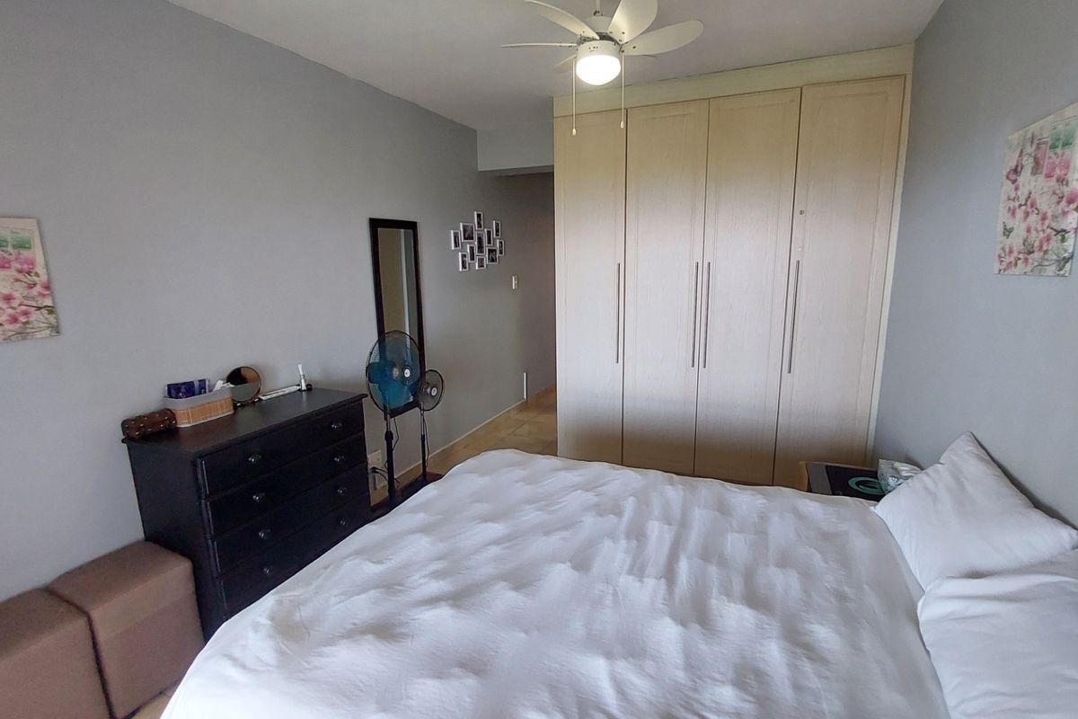 A bedroom featuring neutral wall tones, built-in wooden cupboards for storage, and a ceiling fan.