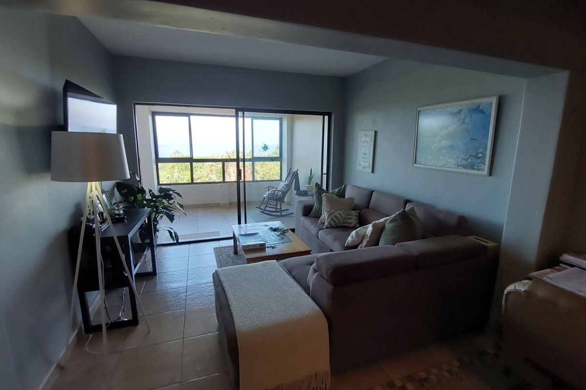 A comfortable living room featuring tiled flooring and large sliding glass doors that provide access to an outdoor balcony area.