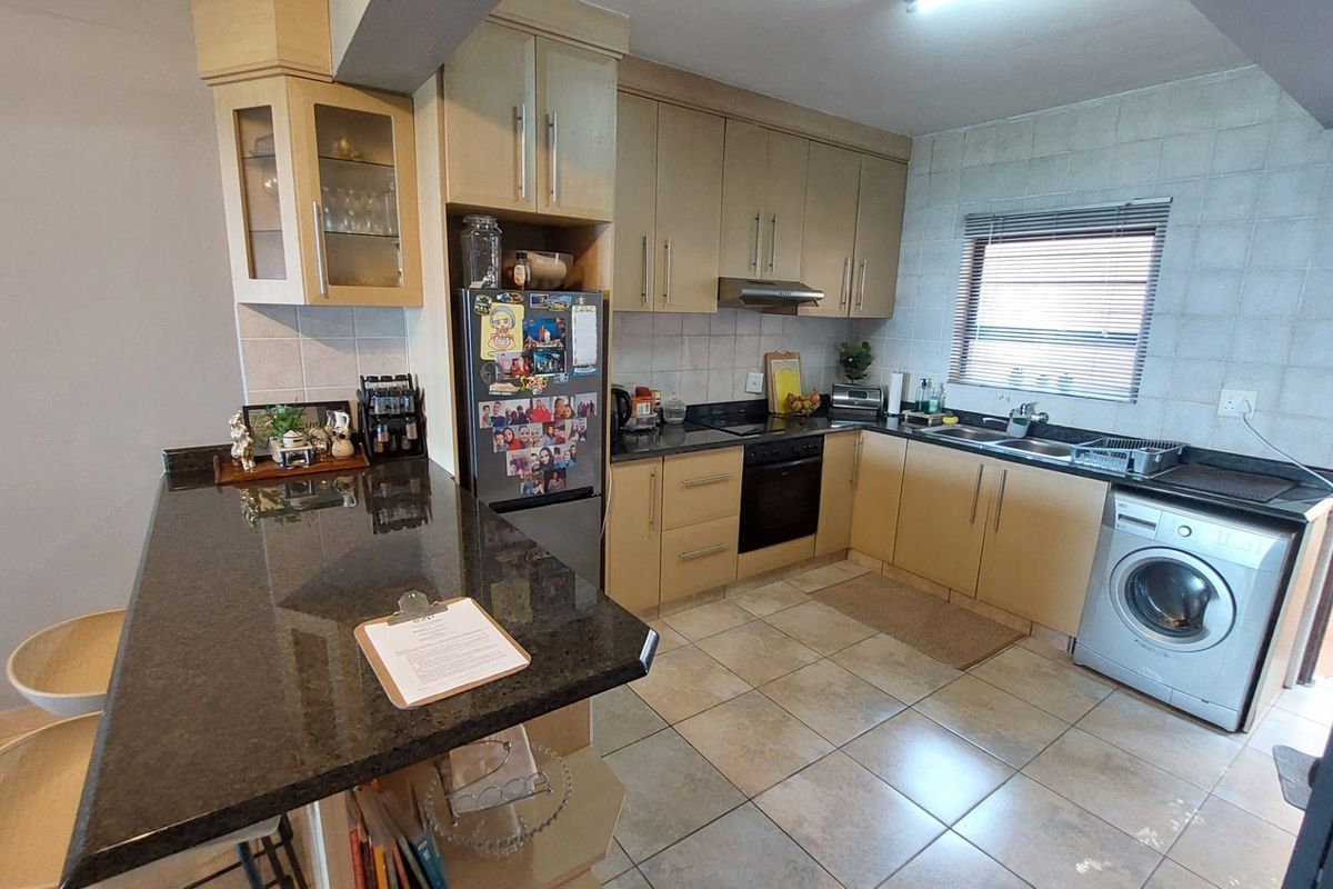 Functional kitchen featuring granite countertops, ample built-in cabinetry, integrated oven, extractor fan, and a double basin sink with tiled flooring and backsplash.