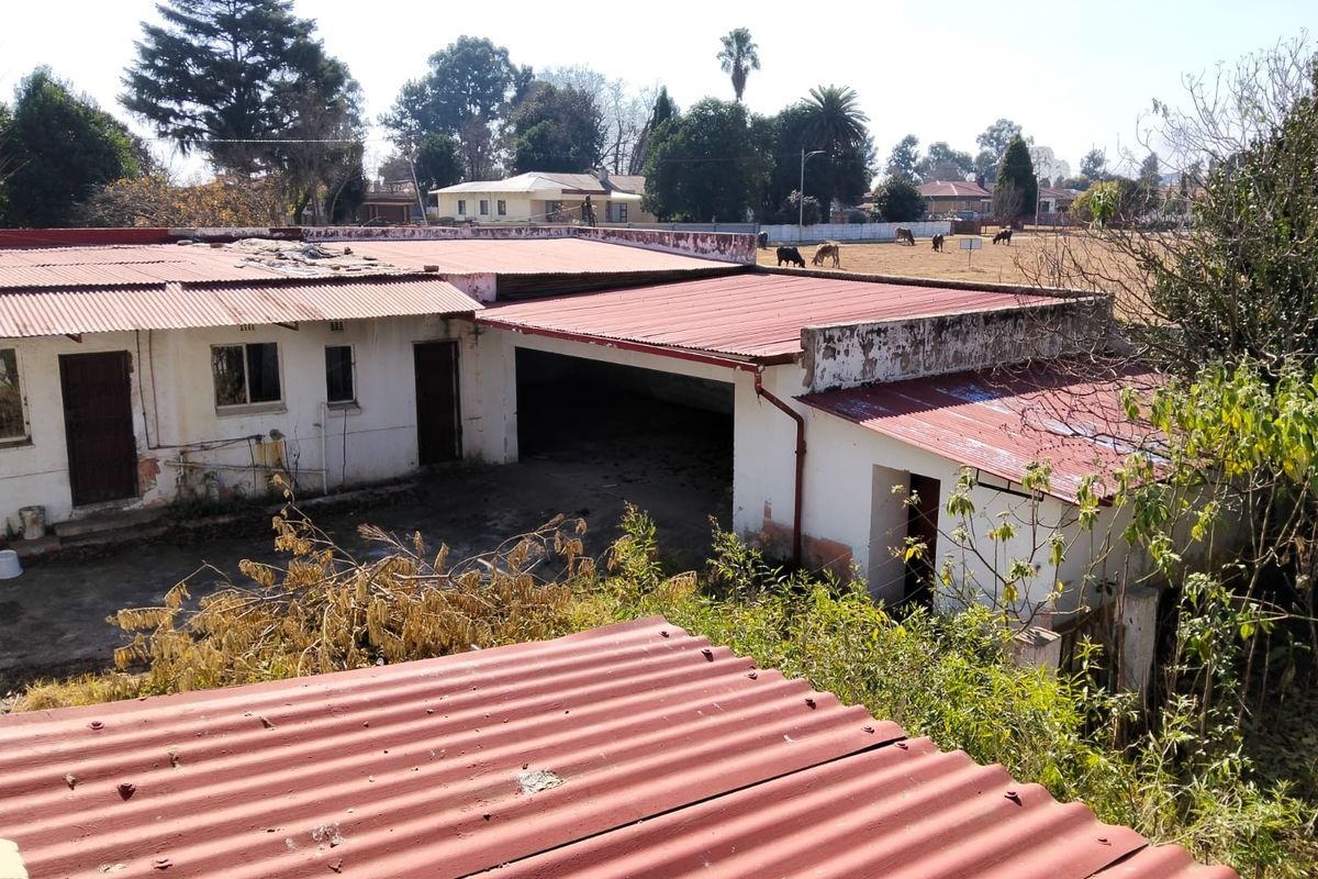 Rear view of the property showing a large open garage area and corrugated metal roofing with visible signs of exterior wear and maintenance needs.