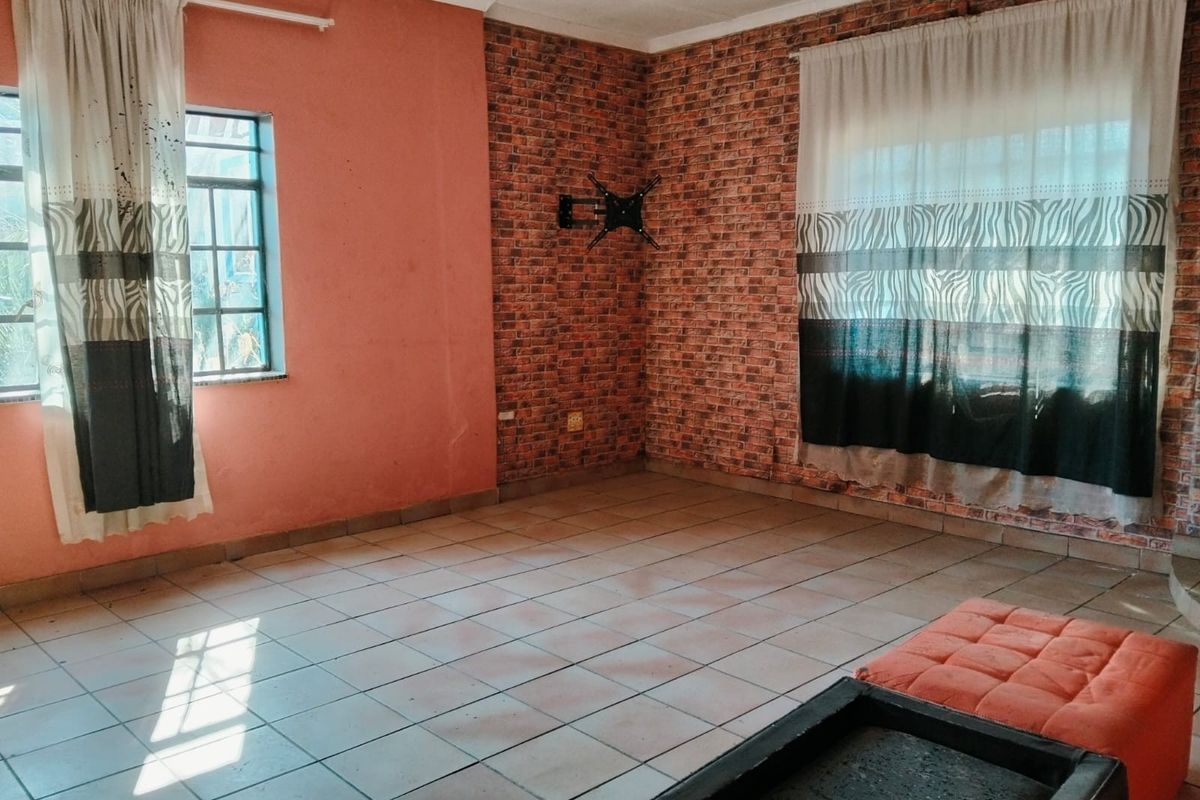 A spacious living area featuring tiled flooring and a brick-effect feature wall, providing a blank canvas for potential interior design updates.