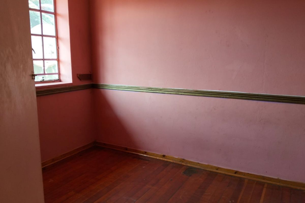 An empty bedroom featuring original timber flooring, a classic window, and decorative chair rail molding, ready for a fresh update.