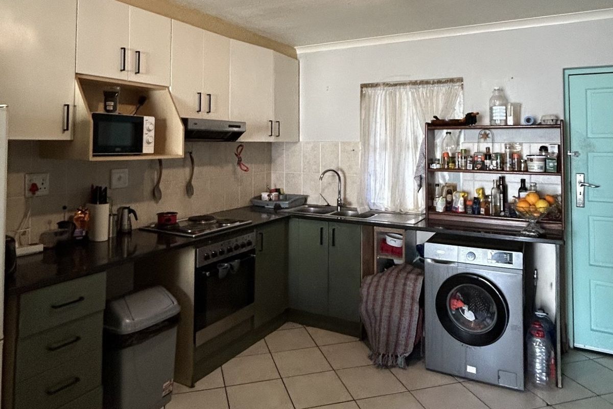 A functional kitchen featuring built-in cabinetry, a tiled backsplash, integrated oven and hob, and tiled flooring with space for laundry appliances.