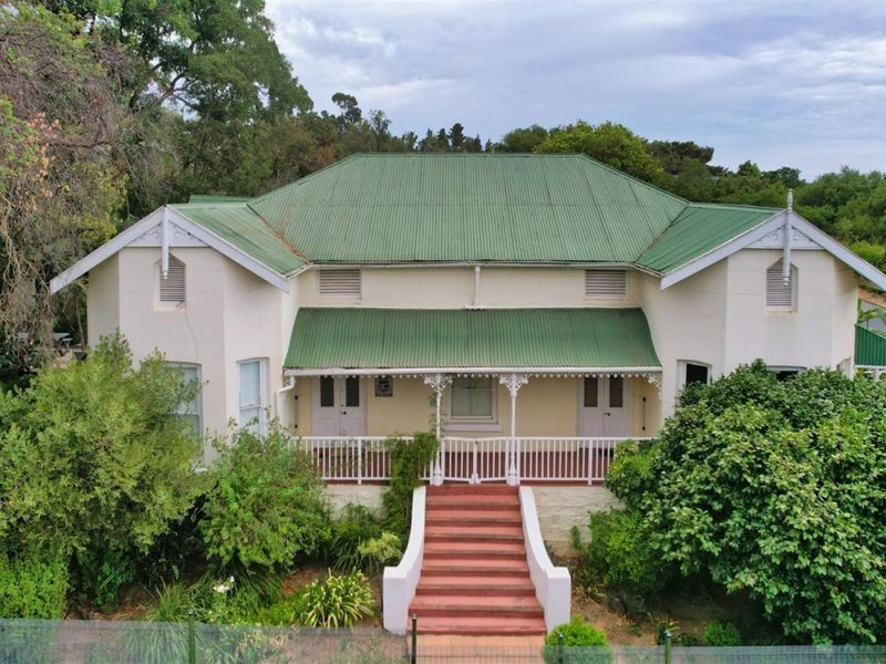 A charming historic-style house featuring a green corrugated metal roof, a covered front veranda with decorative ironwork, and a central concrete staircase.