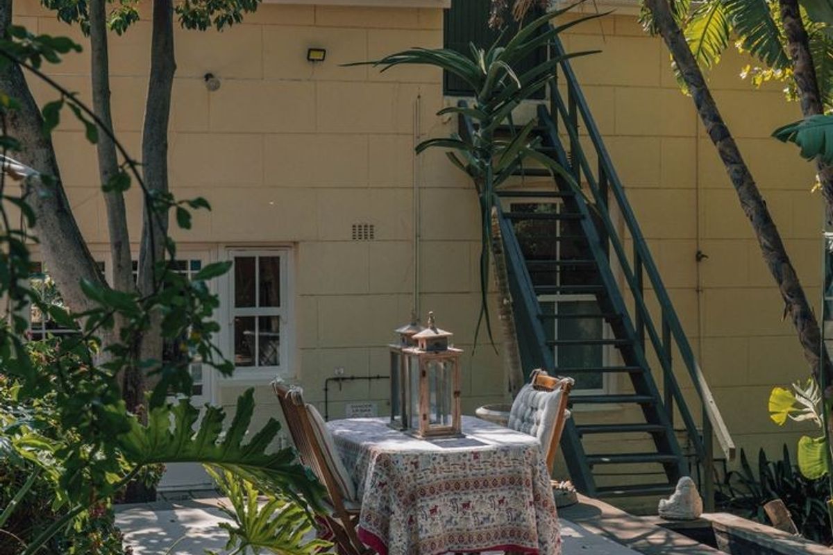 A rear exterior view of the property featuring a concrete patio, an external staircase leading to the upper level, and mature garden landscaping.