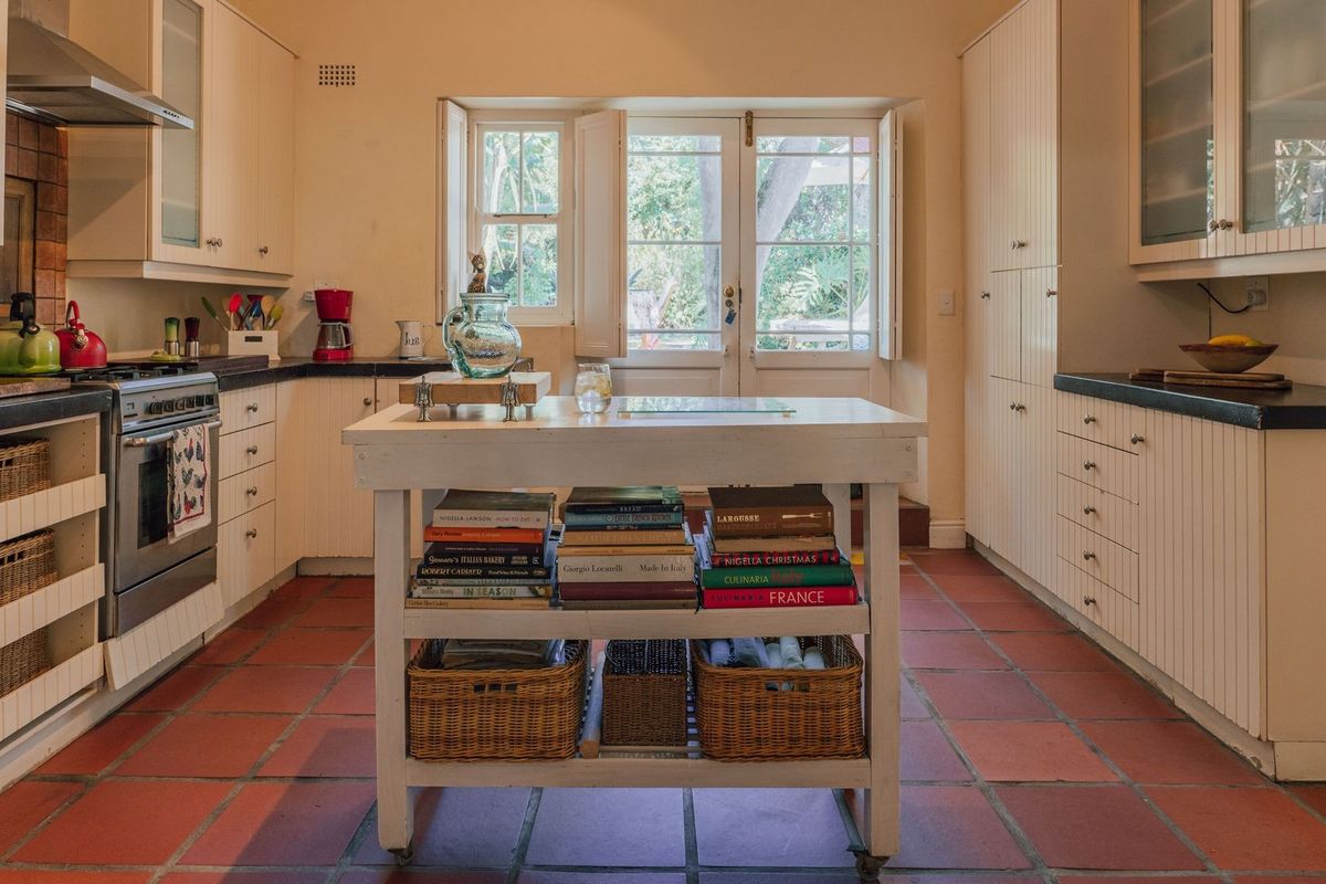 A traditional kitchen featuring built-in cabinetry, a gas stove with extractor fan, terracotta flooring, and direct access to the garden through glass doors.