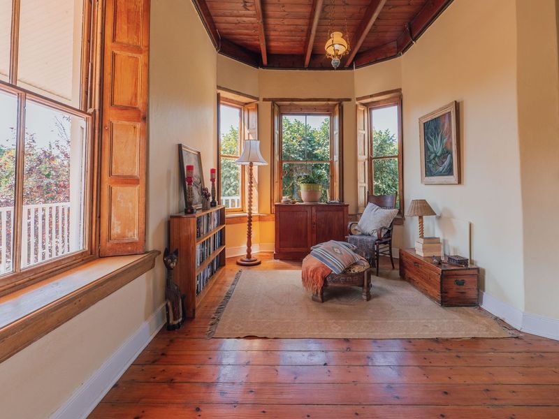 A charming living area featuring warm timber flooring, exposed ceiling beams, and a classic bay window with timber shutters, offering a cozy and character-filled space.