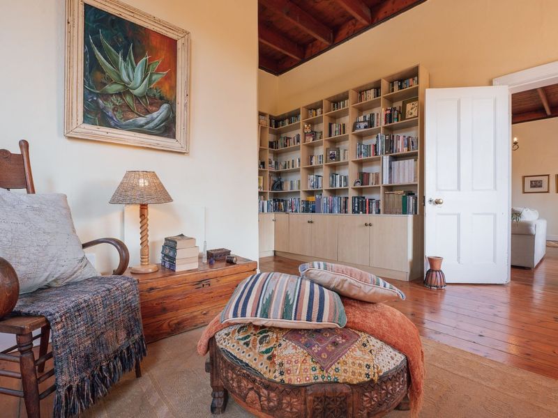 A cozy living room featuring warm timber floorboards, exposed ceiling beams, and extensive built-in floor-to-ceiling bookshelves.