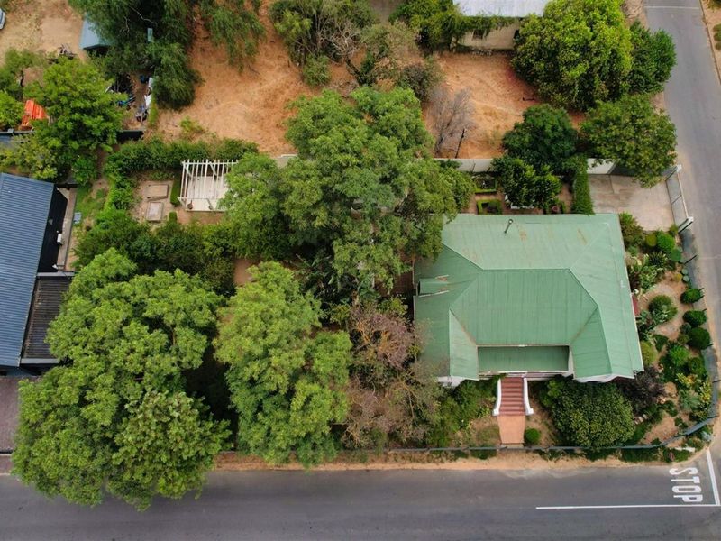 Aerial view of the property showcasing the main house with a green metal roof, swimming pool, pergola, and established garden surroundings.