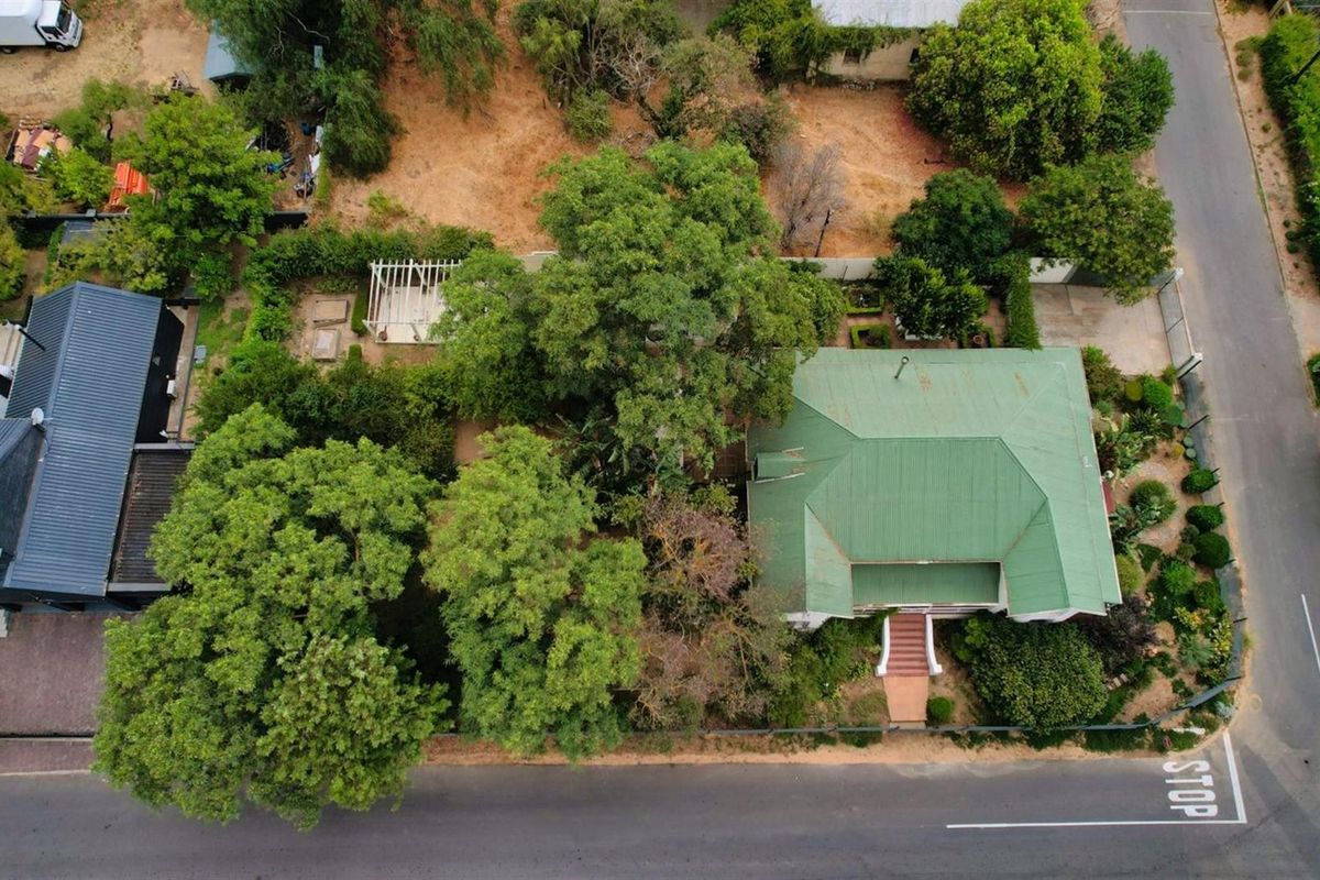 Aerial view of the property showcasing the main house with a green metal roof, swimming pool, pergola, and established garden surroundings.