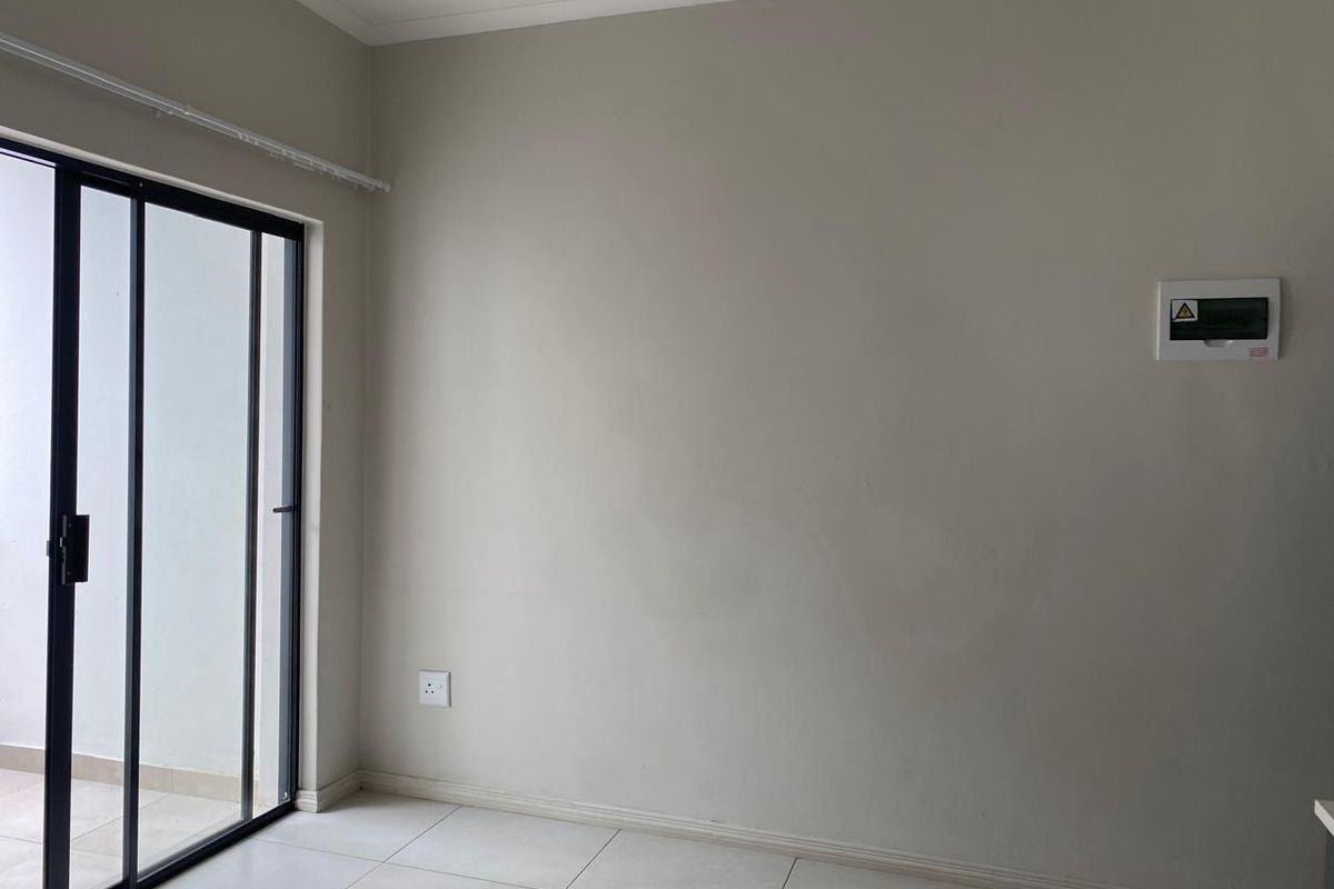 An empty living area featuring tiled flooring, a sliding glass door leading to an outdoor space, and a wall-mounted electrical distribution board.