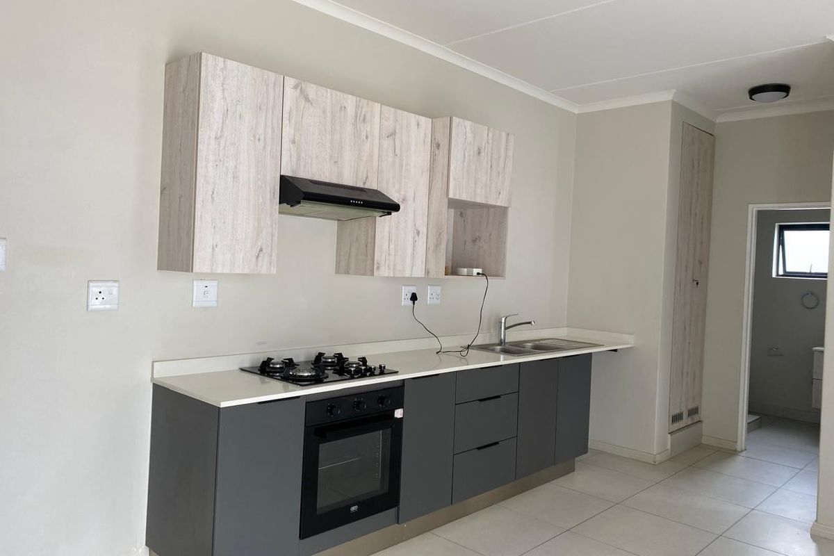 Modern kitchen featuring grey base cabinets, light wood-look upper cupboards, gas hob, built-in oven, and stone countertops with a stainless steel sink.