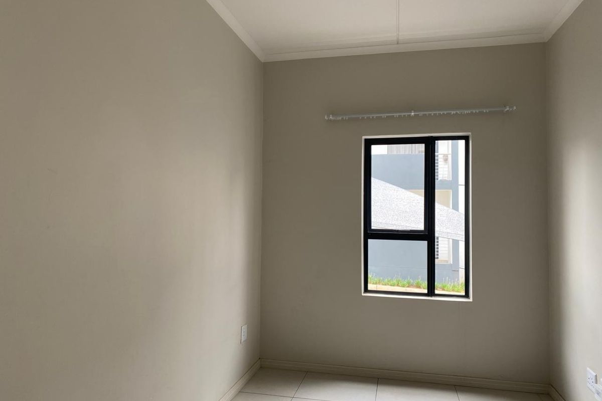 A clean, empty bedroom featuring neutral wall paint, tiled flooring, and a modern aluminium window frame with an installed curtain rail.