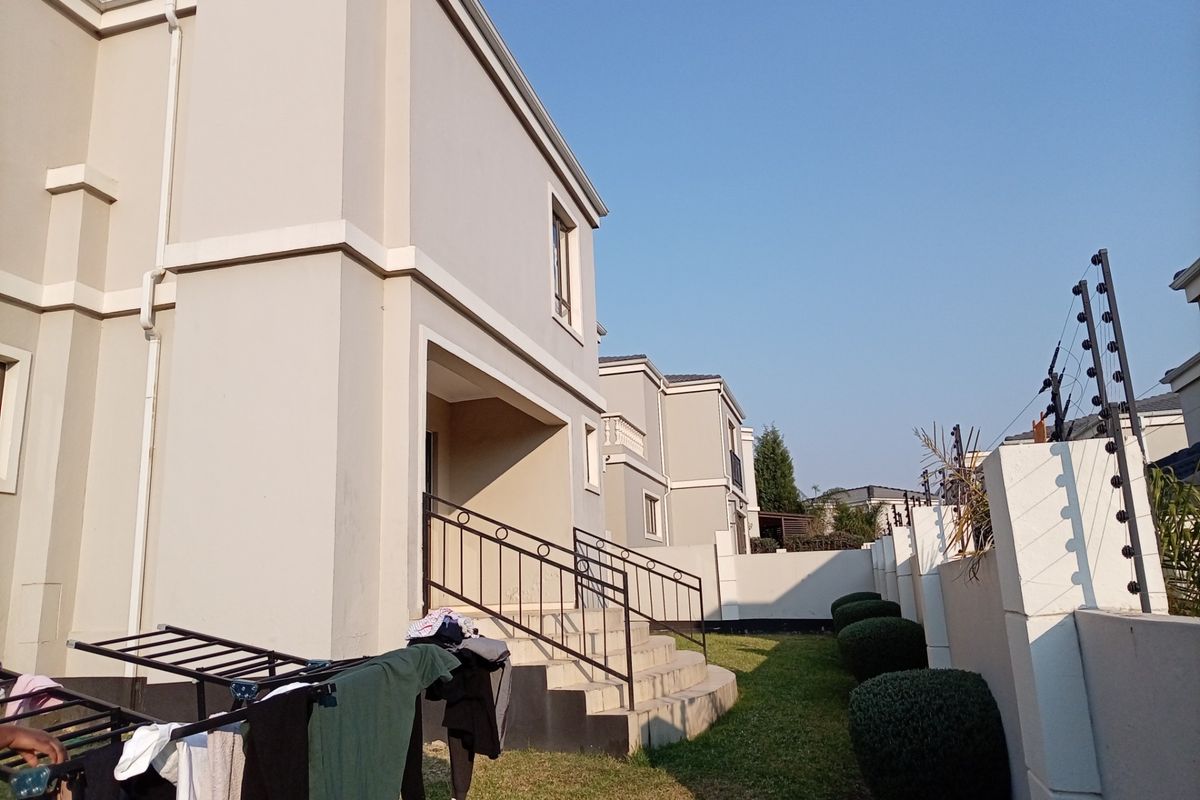 Rear view of the property showing a concrete boundary wall with electric fencing, landscaped garden area, and external staircase access.