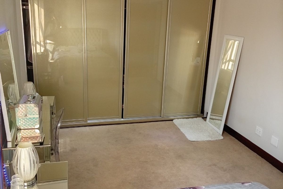 A well-maintained bedroom featuring neutral carpeting, recessed ceiling lighting, and a large built-in wardrobe with sliding doors.