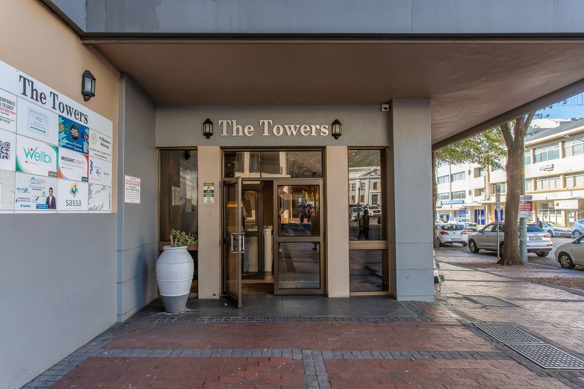 Main entrance to The Towers commercial building, featuring glass doors, covered canopy, and prominent building signage on a paved street-level approach.