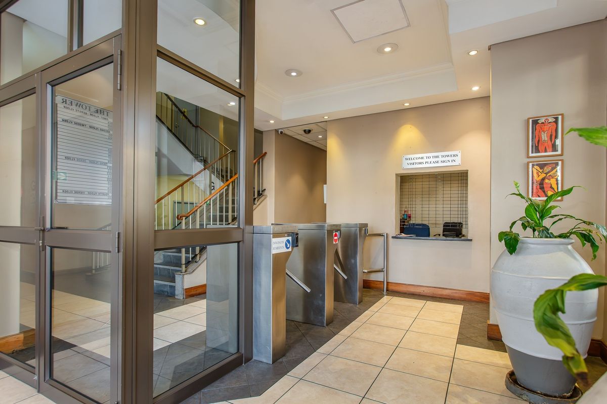 Commercial building entrance lobby featuring security turnstiles, a reception service window, and a staircase leading to upper levels.