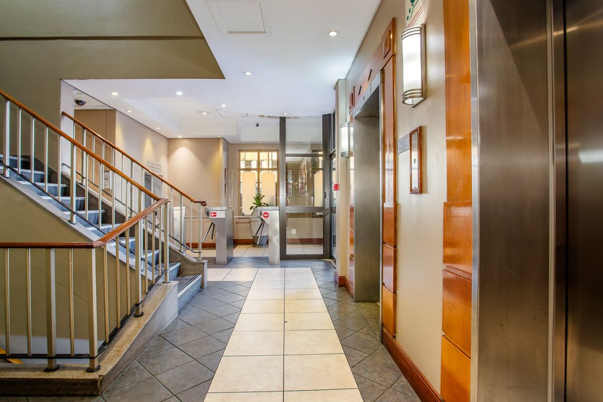 A well-maintained commercial building lobby featuring a staircase, elevator access, and security turnstiles with modern tiled flooring and professional lighting.