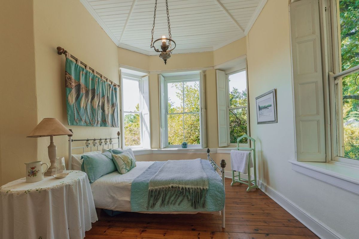 A charming bedroom featuring classic timber flooring, a distinctive bay window with internal shutters, and a high tongue and groove ceiling.