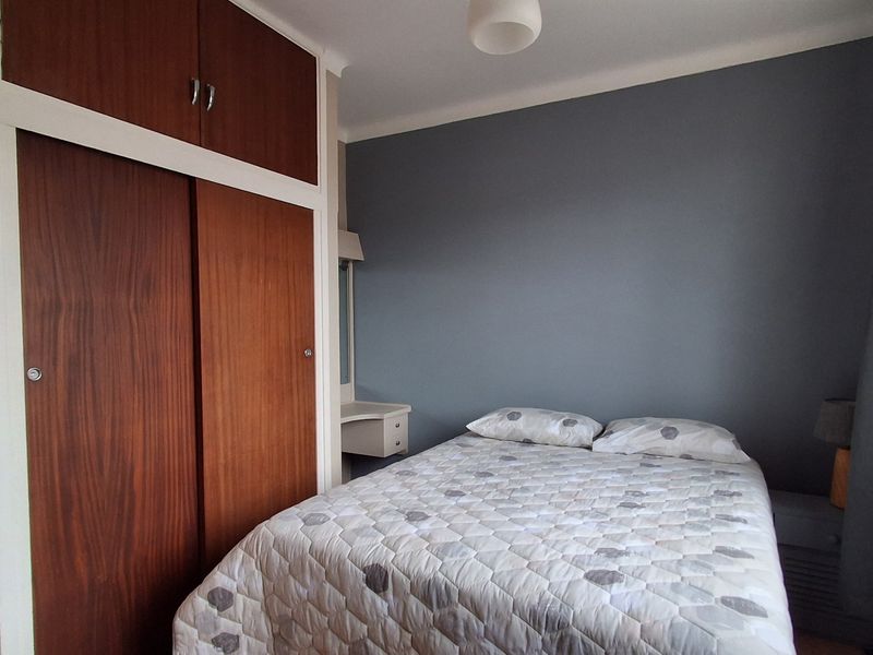 A bedroom featuring a built-in wooden wardrobe and a small integrated vanity unit, finished with a blue accent wall.