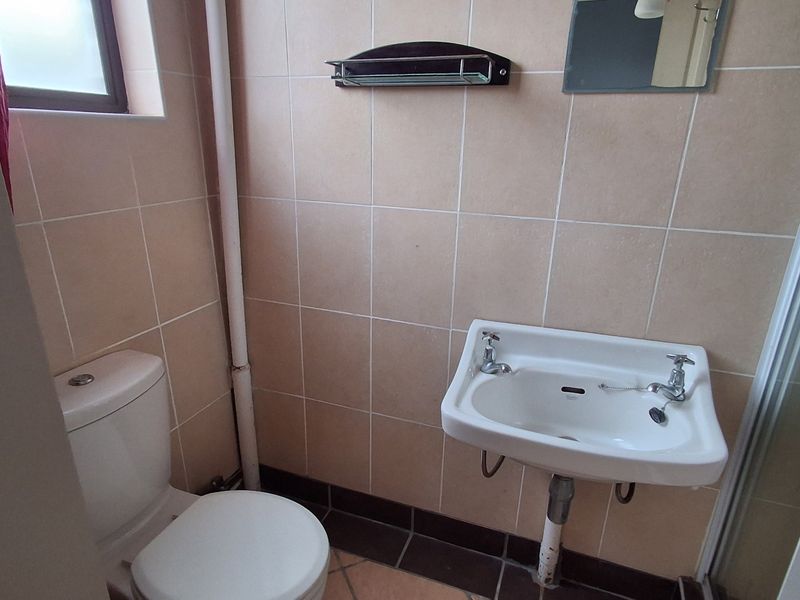 A functional bathroom featuring a wall-mounted basin, close-coupled toilet, and a shower enclosure with neutral ceramic wall and floor tiling.