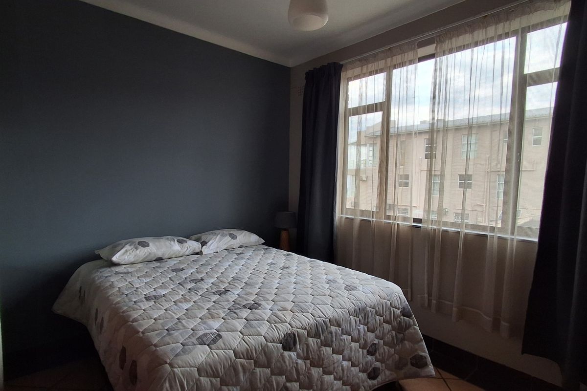 A bedroom featuring a large window with natural light and a dark accent wall, providing a comfortable and functional living space.