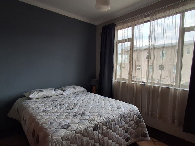 A bedroom featuring a large window with natural light and a dark accent wall, providing a comfortable and functional living space.