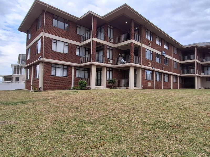 Rear view of a multi-story brick apartment building featuring private balconies and a large communal lawn area.