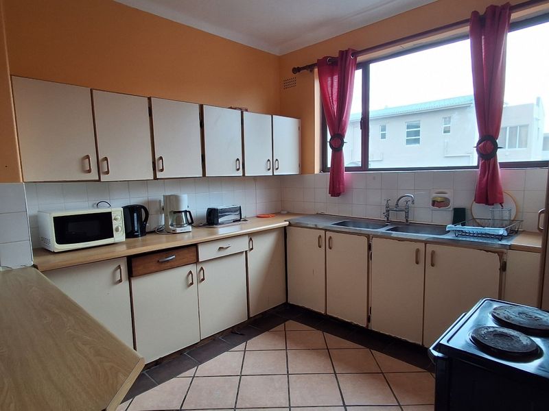 A functional kitchen featuring built-in cabinetry, laminate countertops, a double basin sink, and tiled flooring, offering potential for modernization.