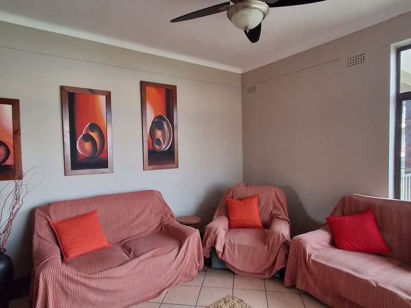 A comfortable living room featuring tiled flooring, a ceiling fan, and a large window providing natural light.