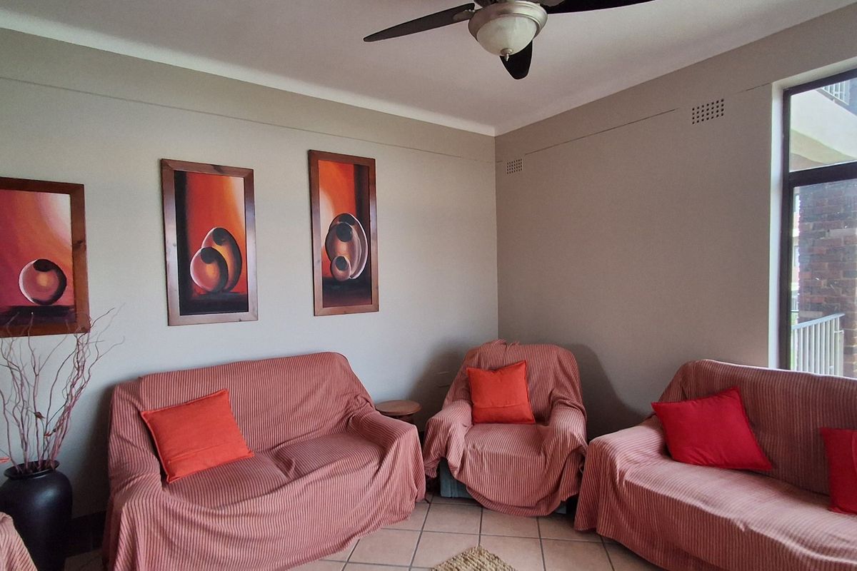 A comfortable living room featuring tiled flooring, a ceiling fan, and a large window providing natural light.