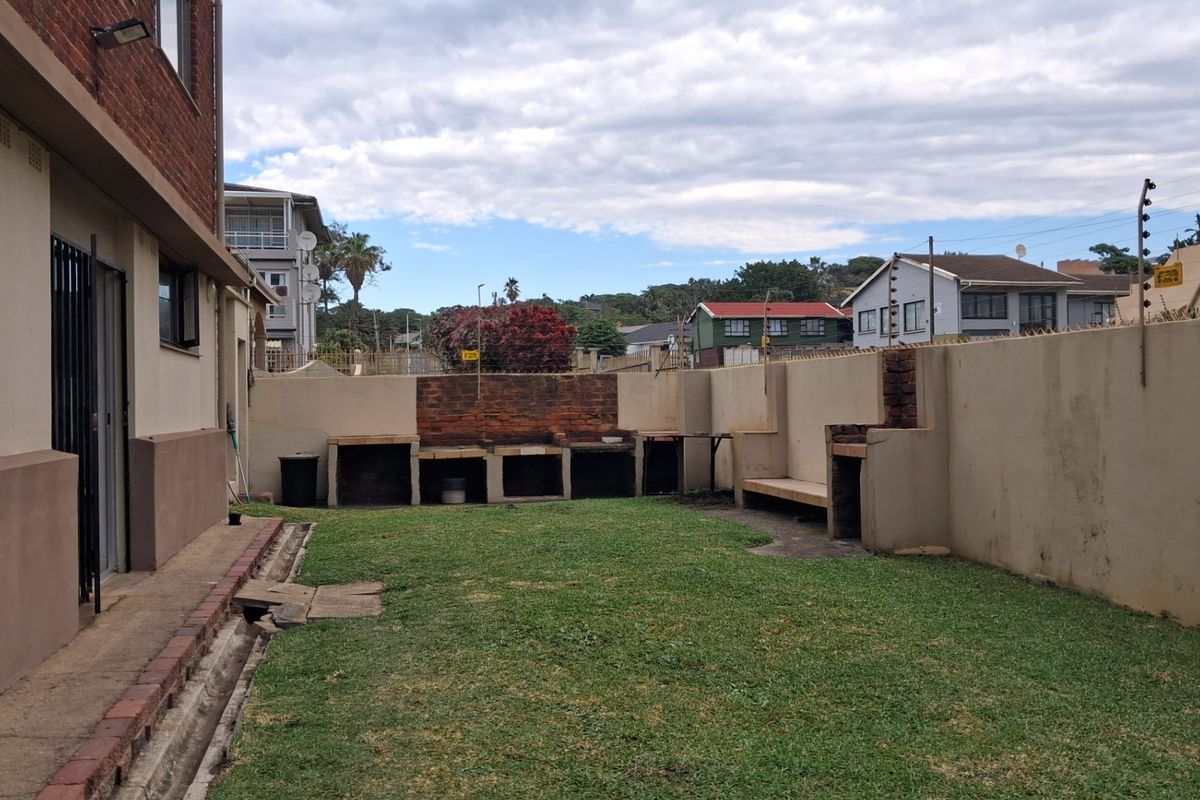 Rear garden area featuring a built-in brick braai station, perimeter wall with electric fencing, and a paved walkway along the building exterior.