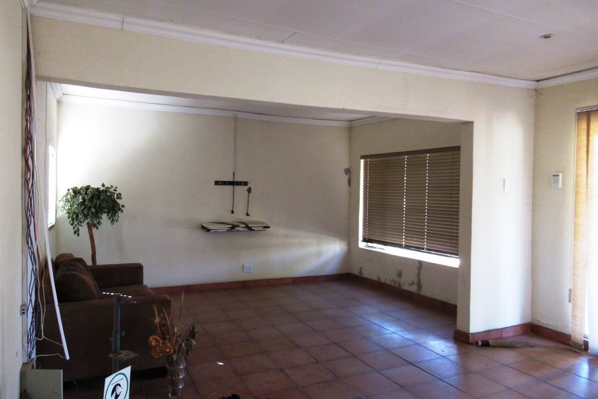 A living area featuring tiled flooring and venetian blinds, showing signs of wall dampness and exposed wiring requiring maintenance.