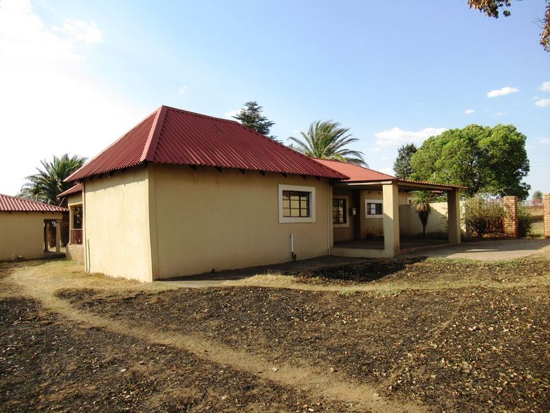 Rear view of a small holding dwelling featuring a corrugated metal roof, covered patio area, and surrounding grounds.