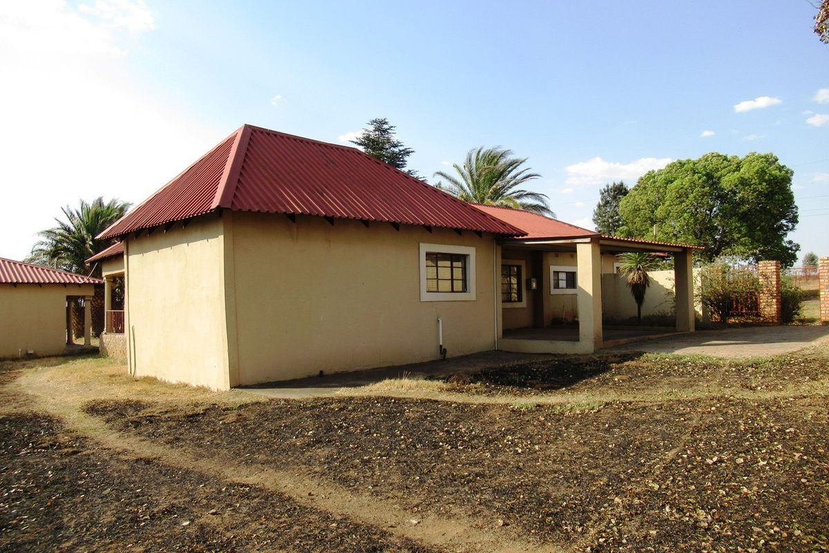 Rear view of a small holding dwelling featuring a corrugated metal roof, covered patio area, and surrounding grounds.