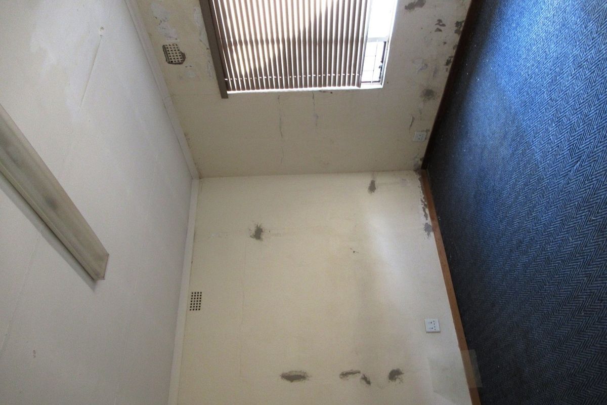 An empty bedroom interior showing significant wall surface damage, peeling paint, and worn flooring, requiring renovation and cosmetic repairs.