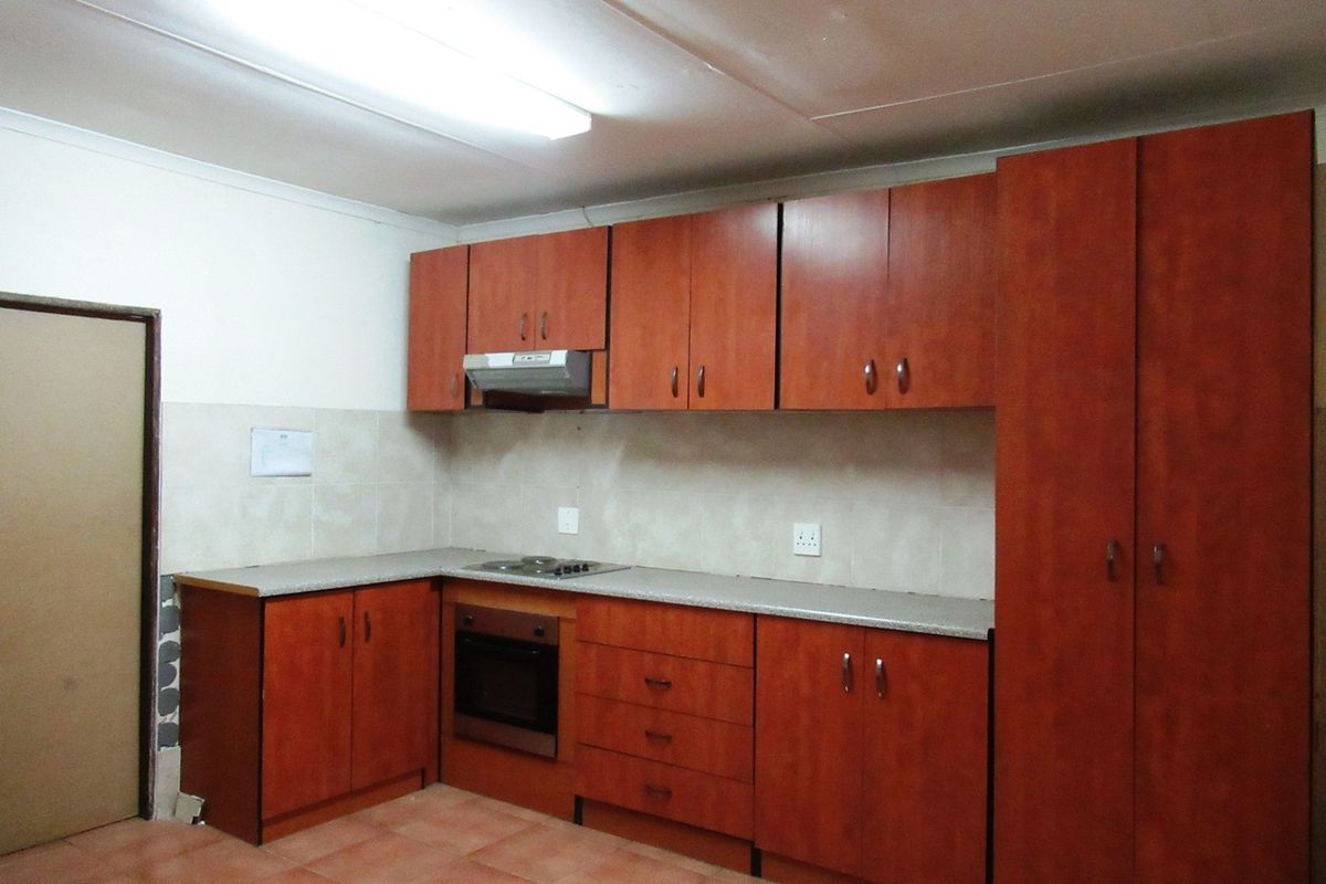 A functional kitchen featuring wooden cabinetry, built-in oven and hob, tiled backsplash, and tiled flooring, offering a clean and practical workspace.