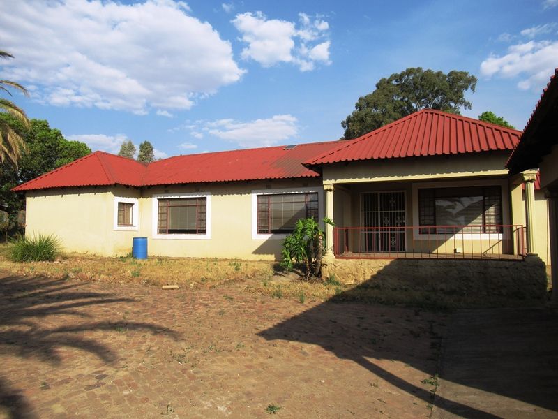 Rear view of a single-story small holding residence featuring a red corrugated metal roof, a covered patio, and a brick-paved yard area.