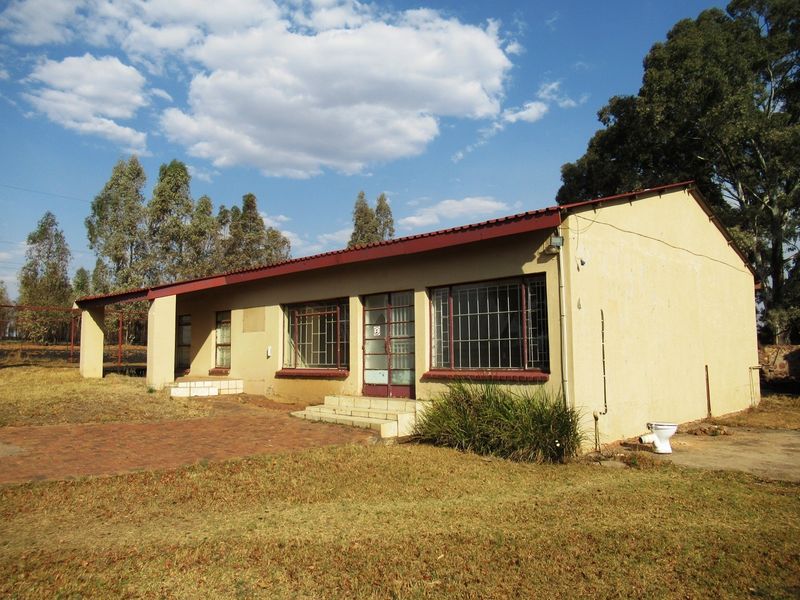 Front elevation of a small holding dwelling featuring a metal roof, security bars on windows, and brick paved entrance area with visible exterior maintenance needs.