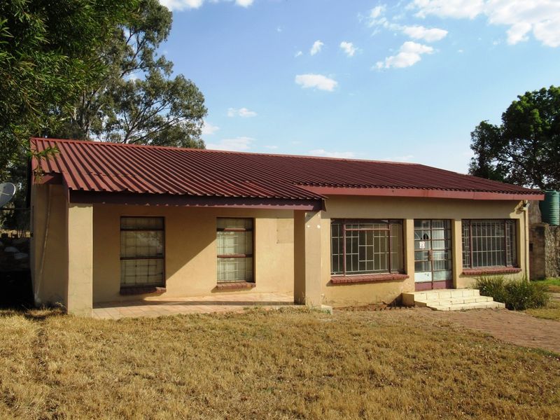 Front view of a single-story small holding dwelling featuring a corrugated metal roof, covered patio, and security bars on windows.