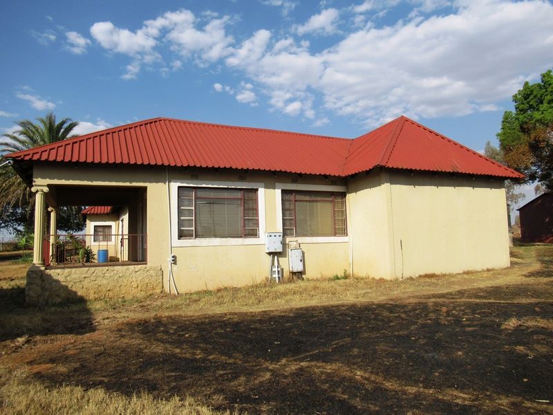 Rear view of a small holding dwelling featuring a red corrugated metal roof, covered patio area, and stone-clad base.