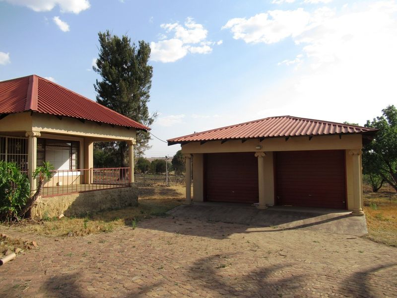 Exterior view of a small holding featuring a double garage with a corrugated roof and an adjacent dwelling with a covered patio area.