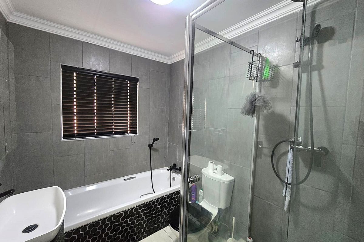 Modern bathroom featuring a bathtub, separate glass-enclosed shower, vessel sink, and contemporary grey tiling with a decorative hexagonal tiled bath surround.