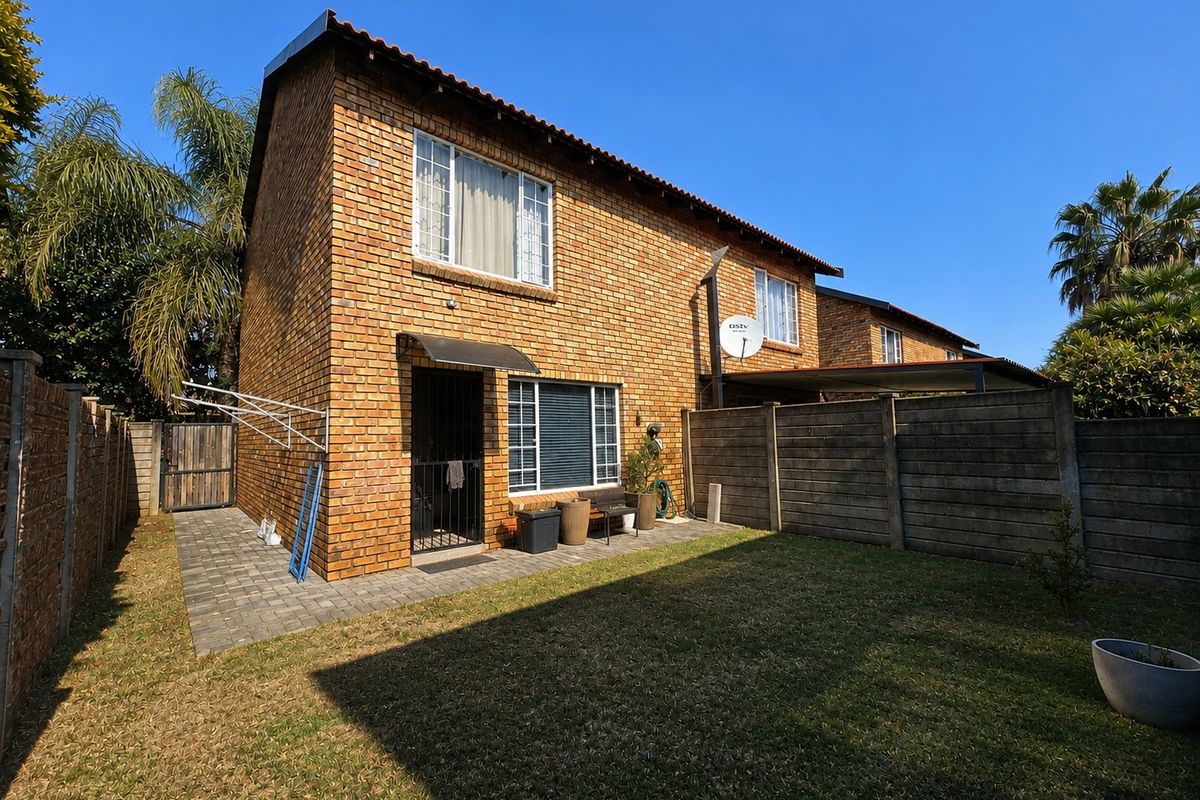 Rear view of a face brick townhouse featuring a private garden, paved patio area, and secure boundary walling.