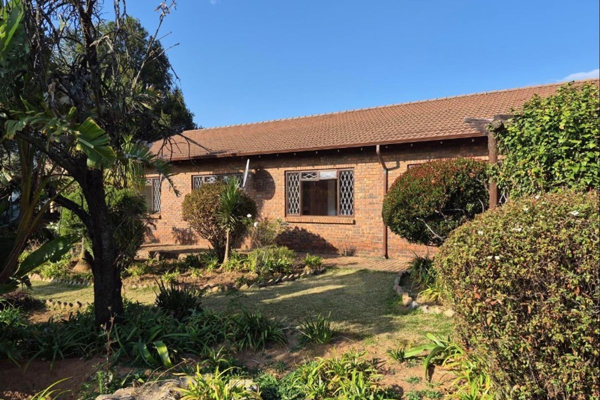 A rear view of a face brick house featuring a tiled roof, diamond-patterned windows, and a surrounding garden with a paved walkway.