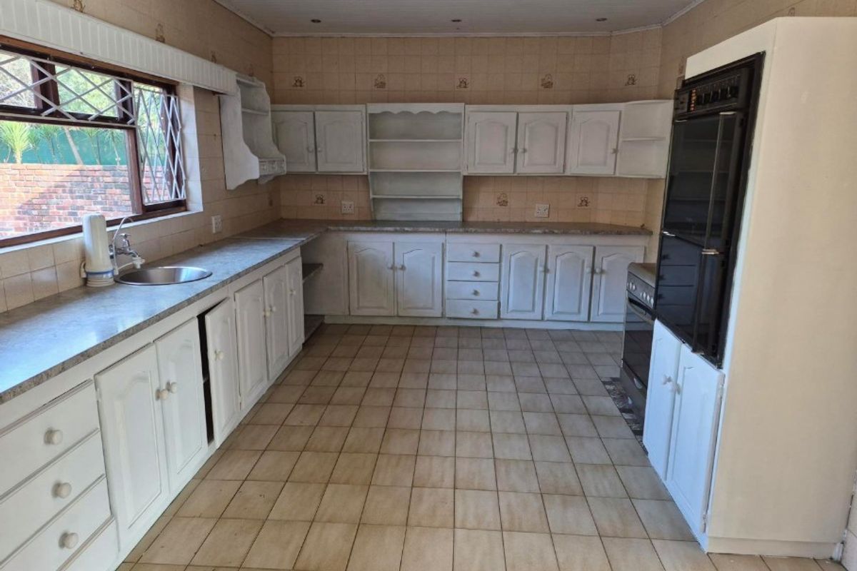 A spacious, dated kitchen featuring white built-in cabinetry, laminate countertops, a built-in oven, and tiled flooring throughout.